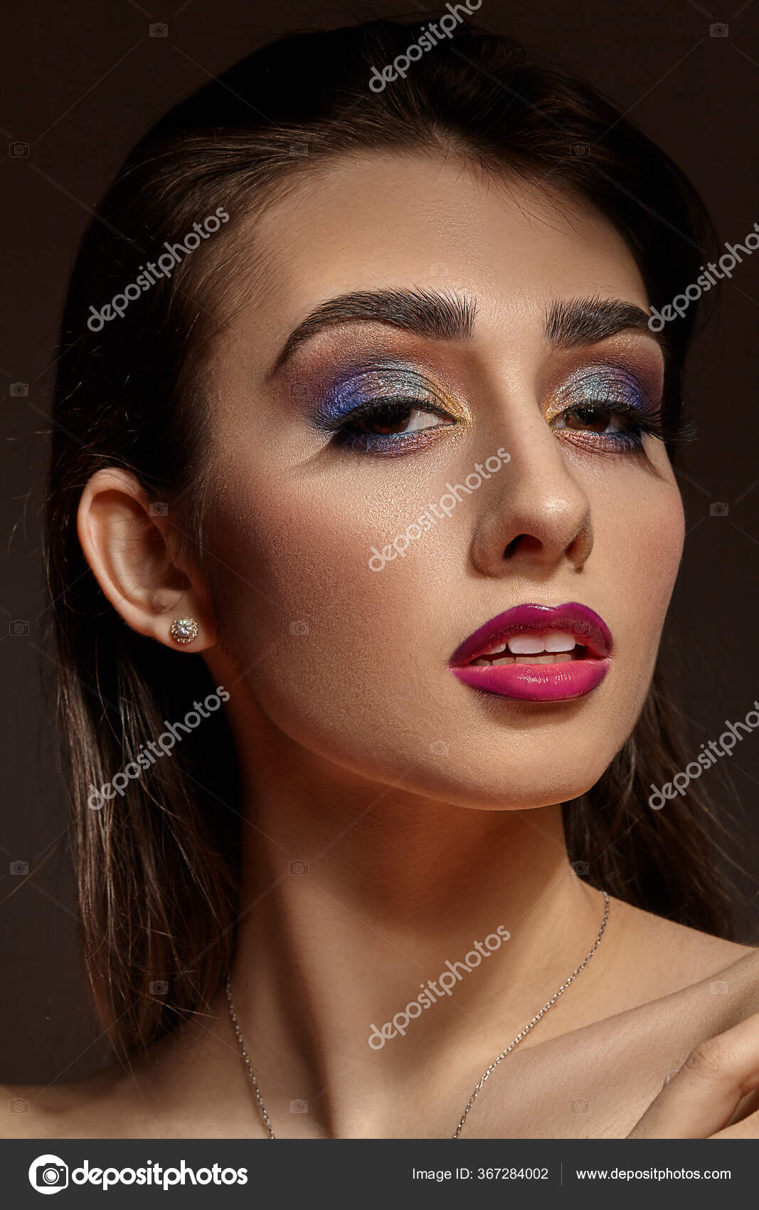 Naked model in necklace and earrings posing on gray background. Bright