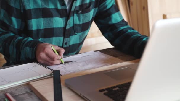 Tesař práce ve své dílně pro kreslení zařízení, papír, pravítko, tužka a laptop — Stock video
