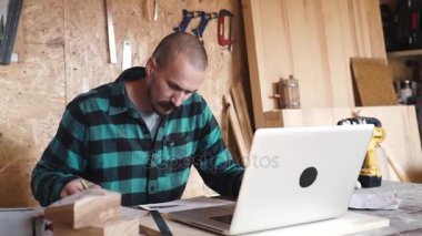 Vintage bıyıklı kalın marangoz atölyesinde çalışırken bir laptop kullanıyor
