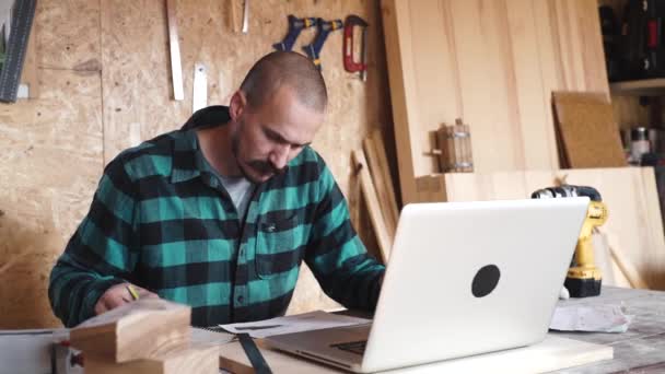 Vet timmerman met vintage snor is een laptop gebruikt terwijl u werkt in de workshop — Stockvideo