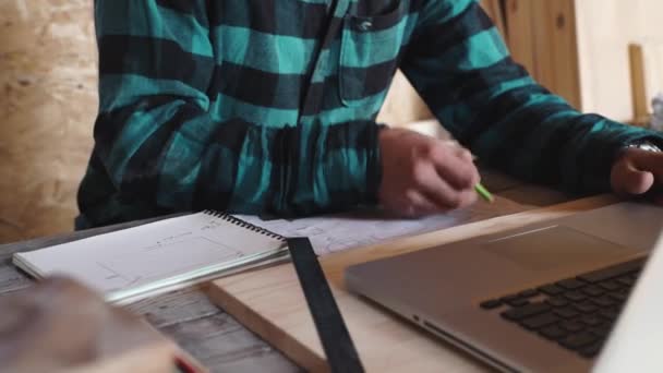 Timmerman werk in zijn werkplaats met de opstelling van de apparatuur, papier, liniaal, potlood en laptop — Stockvideo