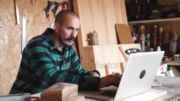 Audace con i baffi giovane falegname artigiano fare disegno con computer portatile nel suo laboratorio di legno — Video Stock