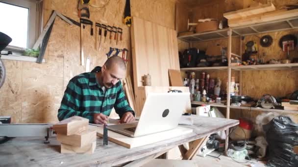 大胆的小胡子的肖像退休木匠坐在他的工作室和使用笔记本电脑。小型企业. — 图库视频影像