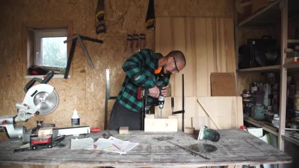 Профессия, люди, плотницкая, деревообрабатывающая и народная концепция - плотник с электродрелью сверлильной доски в мастерской — стоковое видео
