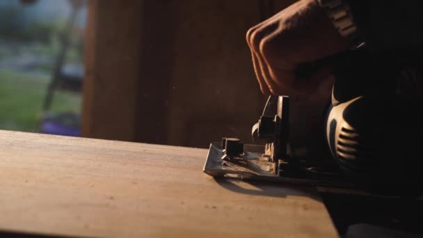 Handen van timmerman met cirkelzaag snijden stuk hout. zon flare op achtergrond — Stockvideo
