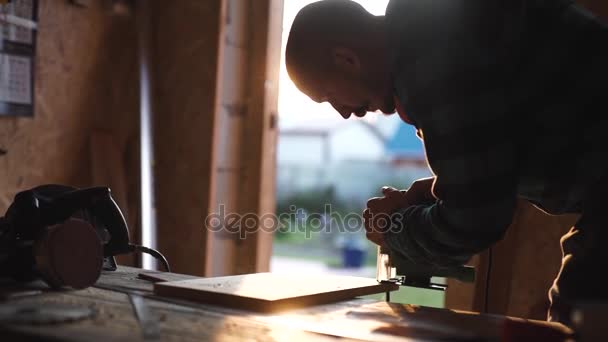 Joven carpintero audaz con bigote. Sierra circular cortando trozos de madera. resplandor solar en el fondo — Vídeo de stock