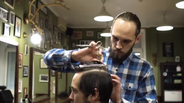 Cabelo longo Barbeiro corta o cabelo do cliente com tesoura e pente em sua barbearia — Vídeo de Stock