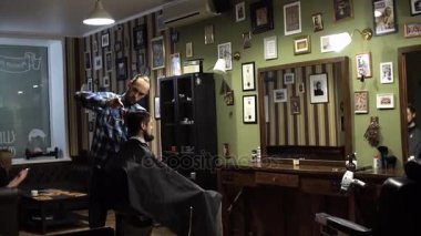 Genç yakışıklı berber berber dükkanında sakallı çekici bir adamın saçını kesiyor.