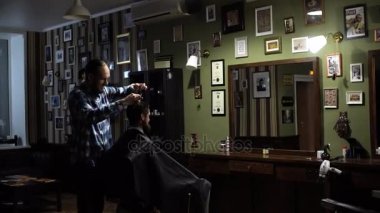 Genç yakışıklı berber berber dükkanında sakallı çekici bir adamın saçını kesiyor.