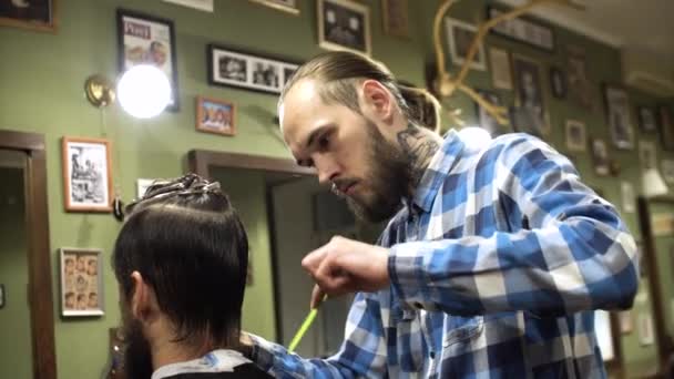 Attrayant jeune coiffeur coupe les cheveux humains avec les ciseaux. Il regarde les cheveux avec concentration. L'homme barbu lève le menton — Video