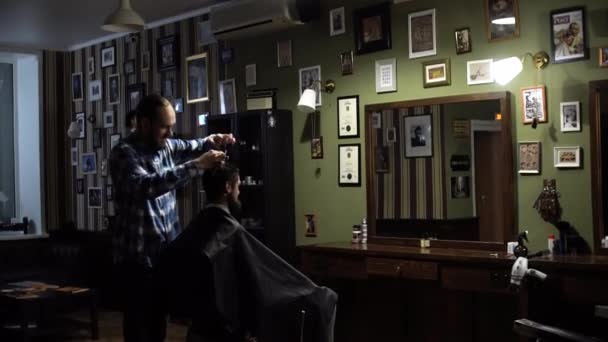 Young handsome barber making haircut of attractive bearded man in barbershop — Stock Video