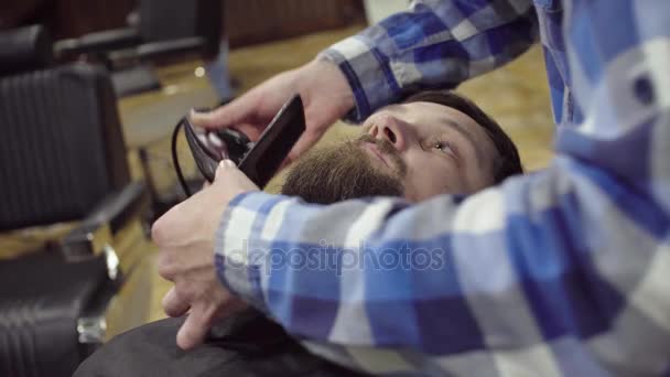 Привлекательный бородатый мужчина сбривает бороду современным парикмахером в парикмахерской — стоковое видео