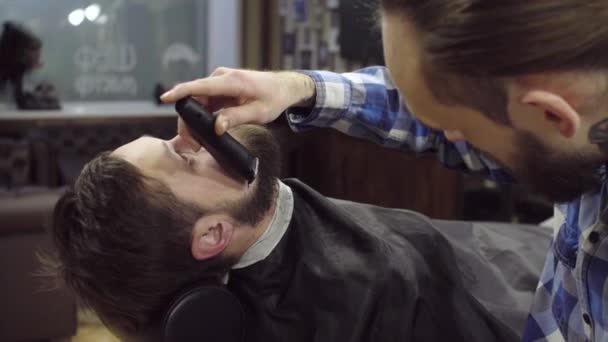 Парикмахерша стрижет бороду клиента клиппером в парикмахерской — стоковое видео