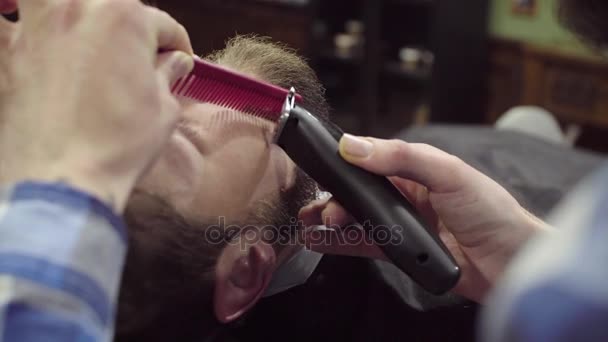 Парикмахерша стрижет бороду клиента клиппером в парикмахерской — стоковое видео