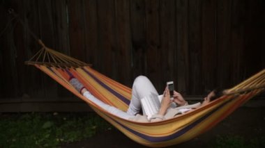 huzurlu bir bahçe içinde yaz tatili sırasında rahatlatıcı ve sallanan bir hamak bir kitap okuma neşeli genç kadın