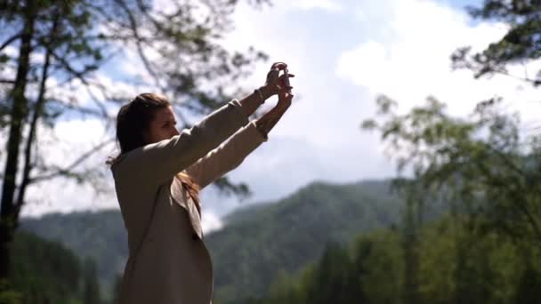 Portrait de jeune femme souriante prenant selfie photo mobile sur la rive de la rivière de montagne dans la journée ensoleillée — Video