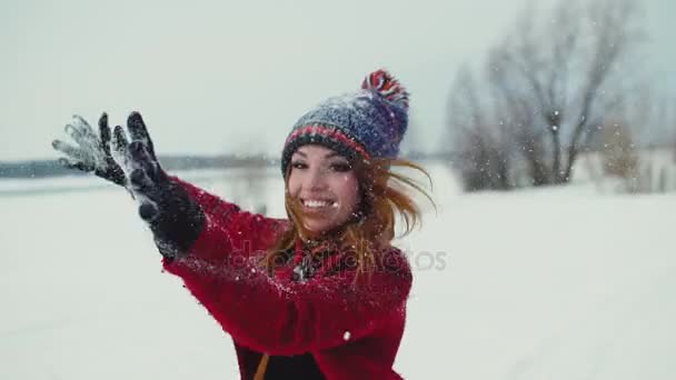 Jovem mulher de cabelo vermelho desfrutando de queda de neve ao ar livre, sorrindo e rindo olhando para a câmera em câmera em câmera lenta 120fps — Vídeo de Stock