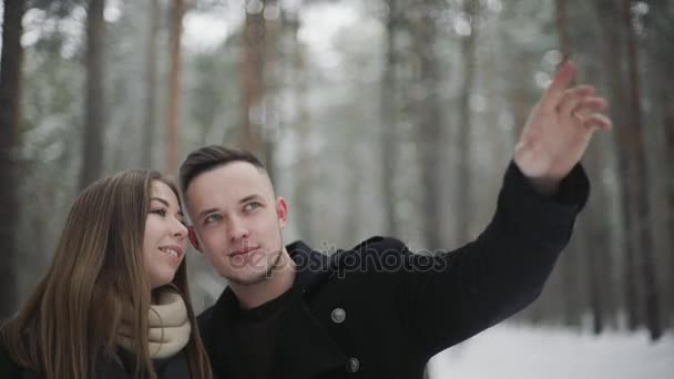 Homem conversando com sua namorada na floresta de inverno e mostra algo ao redor — Vídeo de Stock