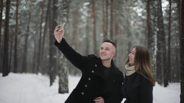 Pareja feliz se toma selfie por teléfono inteligente en un bosque de invierno — Vídeo de stock