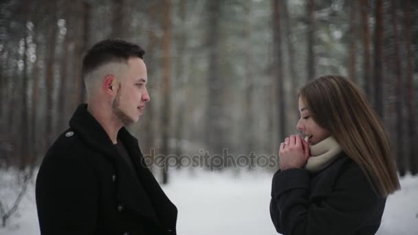 Fiatal pár, a téli erdőben. Az ember lány felmelegíti a kezét az ő lélegzete. — Stock videók