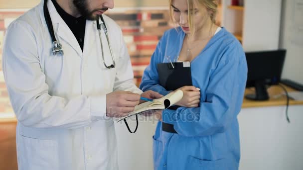30s φαλακρός duscuss γιατρός με 20s ξανθιά νοσοκόμα στην ιατρική στολή στο γραφείο 4k — Αρχείο Βίντεο