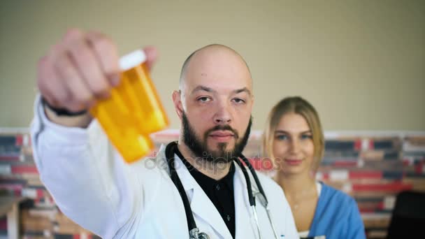 30s łysy lekarz jest daje leków pigułki w słoiku w kamerę i trzęsie 4k — Wideo stockowe