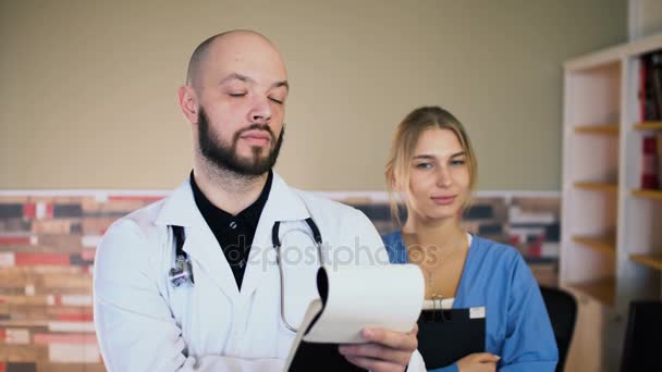 Adulto 30s hombre médico con una enfermera de 20 años en uniforme están posando en el consultorio médico 4k — Vídeo de stock