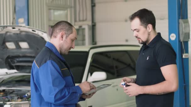 Meccanico che mostra una carta negli appunti a un cliente maschio in un garage — Video Stock