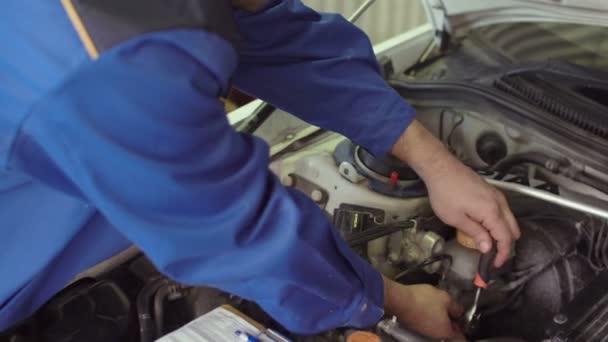 Bilmekaniker i en blå uniform fastställande bil under öppnade huven, diagnostik — Stockvideo