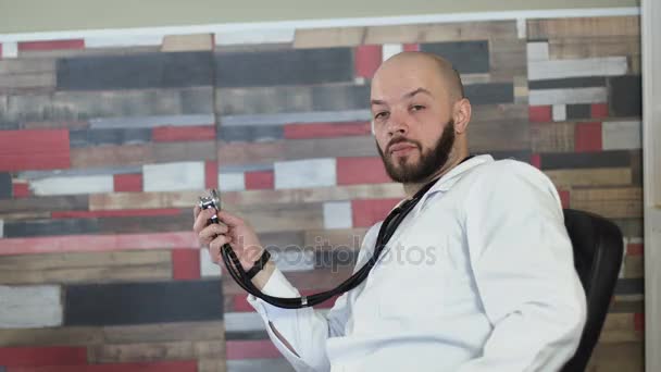 A portrait of a adult 30s bald bearded doctor sitting on his medical room office among table 4k — Stock Video