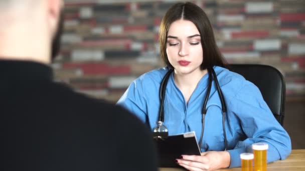 Cita con los médicos: mujer veinteañera trabajador médico de cabello castaño en uniforme azul se discute con el paciente y da medicamentos en tarro naranja 4k — Vídeo de stock