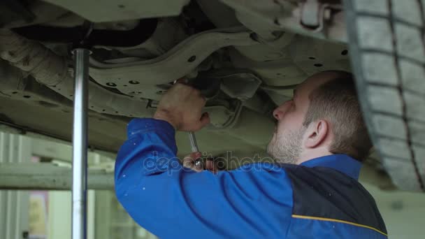 Mecánico del coche está comprobando la suspensión del coche en el coche crossover levantado en monos azules en el taller de reparación de automóviles — Vídeos de Stock