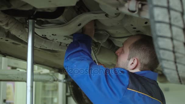 Mecánico del coche está comprobando la suspensión del coche en el coche crossover levantado en monos azules en el taller de reparación de automóviles — Vídeos de Stock