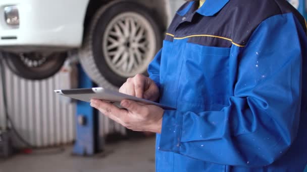 Handen van man auto monteur met tablet met opgeheven auto op achtergrond — Stockvideo