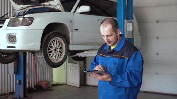 Mecânico de carro dos anos 30 em uniforme azul usando tablet no serviço de reparação de automóveis — Vídeo de Stock