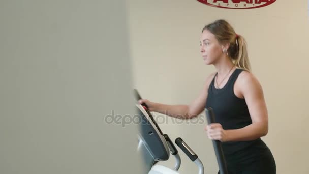 Jolie femme de 20 ans en vêtements de sport en travaillant sur une machine ellipsoïde dans un gymnase — Video