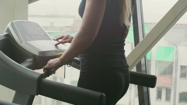 Frau wechselt vor dem Training im Fitnessstudio hinter einem Fenster den Modus des Laufbands — Stockvideo