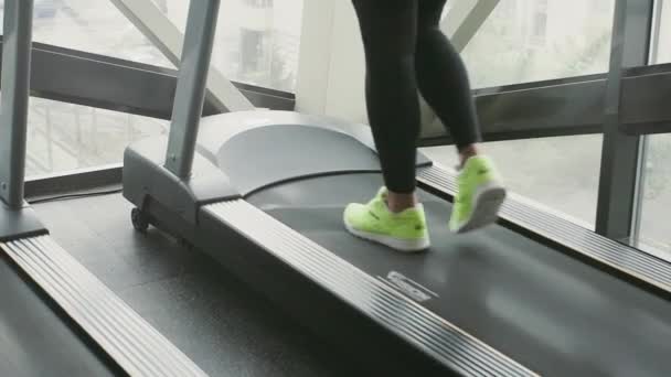 Gros plan des jambes avec des baskets vertes qui courent sur un tapis roulant au ralenti dans un gymnase — Video