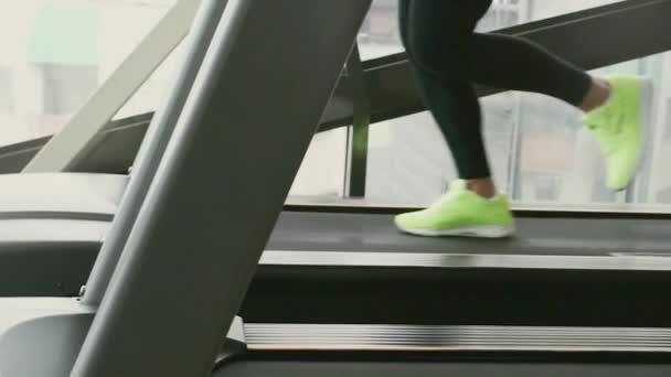 Gros plan des jambes avec des baskets vertes qui courent sur un tapis roulant au ralenti dans un gymnase — Video