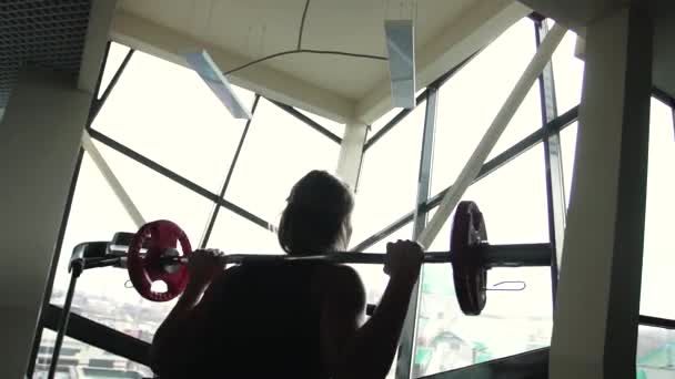 La silhouette di una donna sportiva solleva il bilanciere dietro la finestra in una palestra — Video Stock