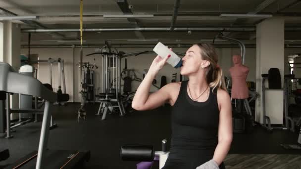 Портрет спортсменки - это питьевая вода со спортивной бутылкой. тренажеры на заднем плане — стоковое видео