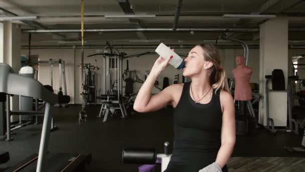 Ritratto di una sportiva è bere acqua con bottiglia sportiva. macchine palestra su sfondo — Video Stock