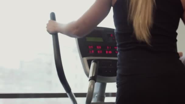 Pretty 20s woman in sportswear in working on ellipsoid machine in a gym — Stock Video