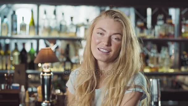 Mulher loira bonita em vestido de noite sentado perto do balcão de bar e olhando para a câmera — Vídeo de Stock