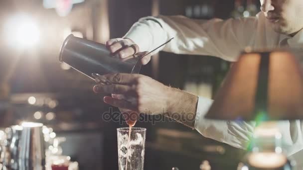 20s barman in een hoed is gemengd cocktail van shaker in een glas gieten — Stockvideo