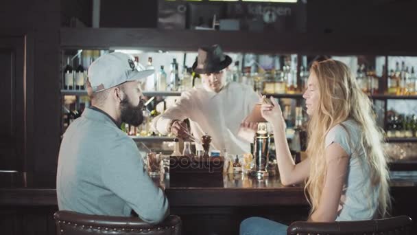 Veinteañeros bonita pareja coqueteando en el bar, clink vasos, barman dando cócteles — Vídeo de stock