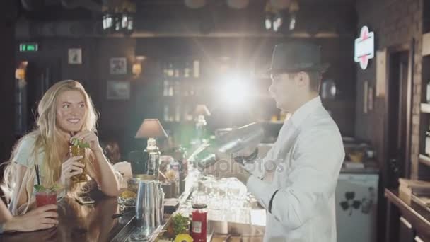 Companhia de 20s amigos estão dring coquetéis enquanto bartender em chapéu está preparando bebidas atrás no bar de festa à noite — Vídeo de Stock
