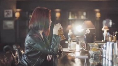 20'li seksi güzellik Kızıl saçlı kadın siyah deri ceketli mi içki kokteyl, kamera ve flört gülümsüyor bardaki bakarak