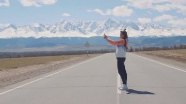 Yalnız kadın turist arka plan üzerinde Dağları ile karayolu otoyol tay iken akıllı telefon üzerinde fotoğraf çekmek