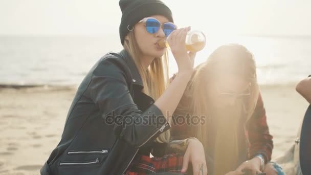 Una chica de 20 años bebe cerveza en la playa durante una puesta de sol en compañía de sus amigos de cerca . — Vídeos de Stock